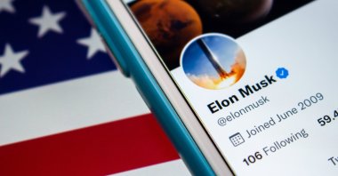 The Twitter account of Elon Musk is seen with the U.S. flag in the background. (Photo by Shutterstock)