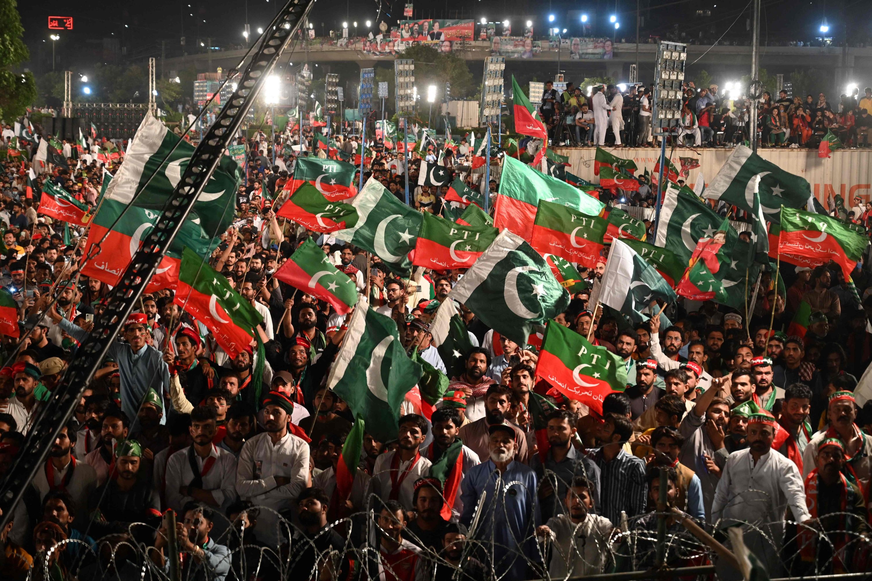 Supporters of Pakistan Tehreek-e-Insaf (PTI) party of former Prime Minister Imran Khan, hold the party and Pakistani flags as they listen to the speech during a rally in Lahore, April 21, 2022. (AFP Photo)