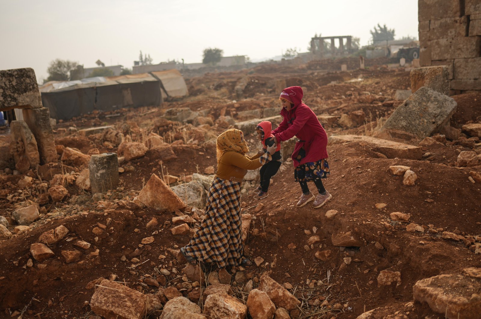 A Syrian woman holds a child next to ancient Roman-era ruins where they have set their tents in Sarmada district, north of Idlib city, Syria, Nov. 25, 2021. (AP File Photo)