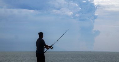 A man fishes at Pasauran beach, Anyer in Serang on April 24, 2022 while Mount Anak Krakatau spews thick smoke into the air. (AFP Photo)