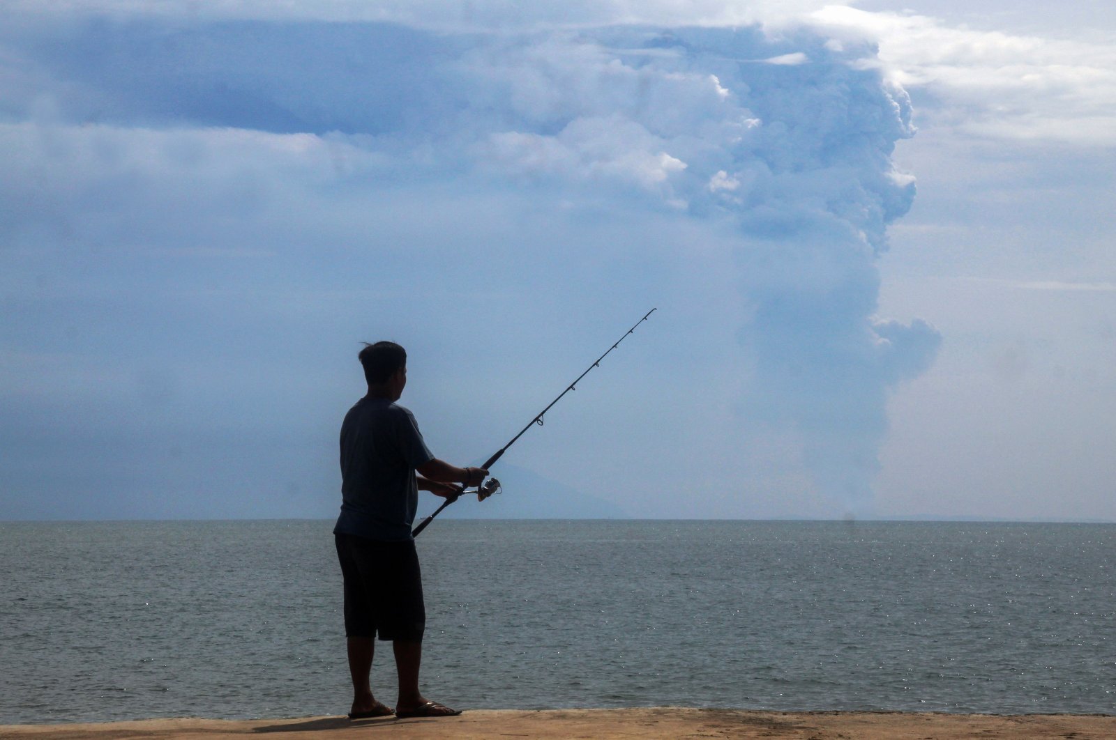 A man fishes at Pasauran beach, Anyer in Serang on April 24, 2022 while Mount Anak Krakatau spews thick smoke into the air. (AFP Photo)