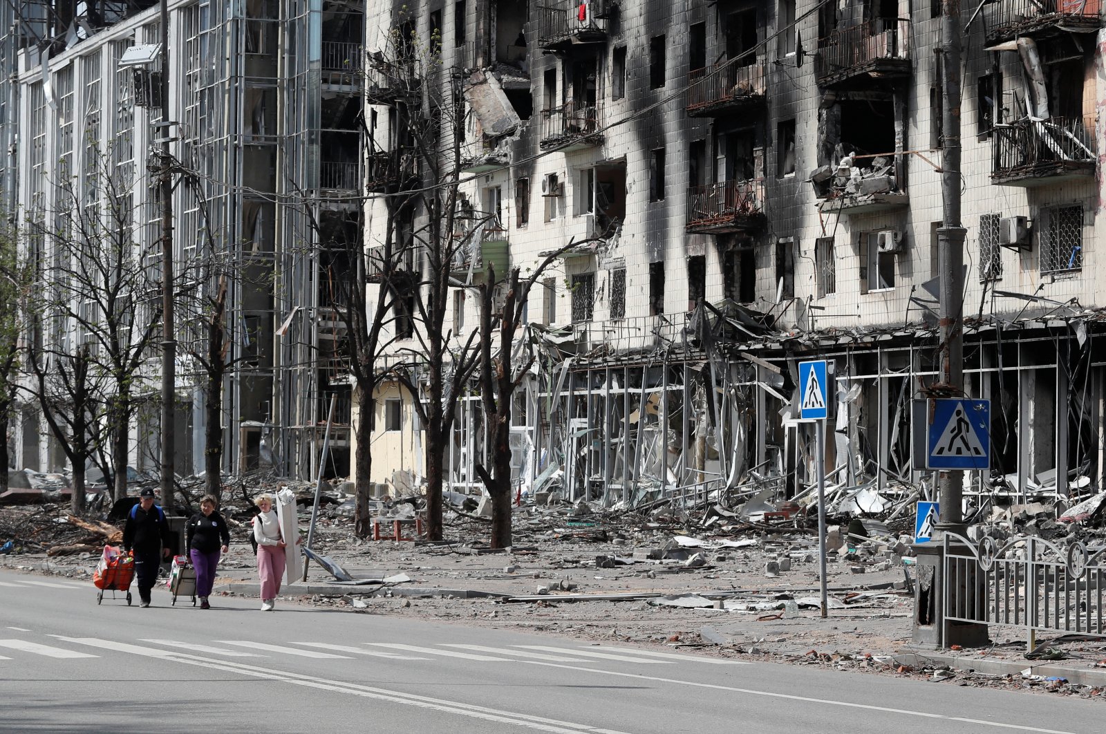 People walk along a street near a building damaged during the Ukraine-Russia conflict in the southern port city of Mariupol, Ukraine, April 25, 2022. (Reuters Photo)