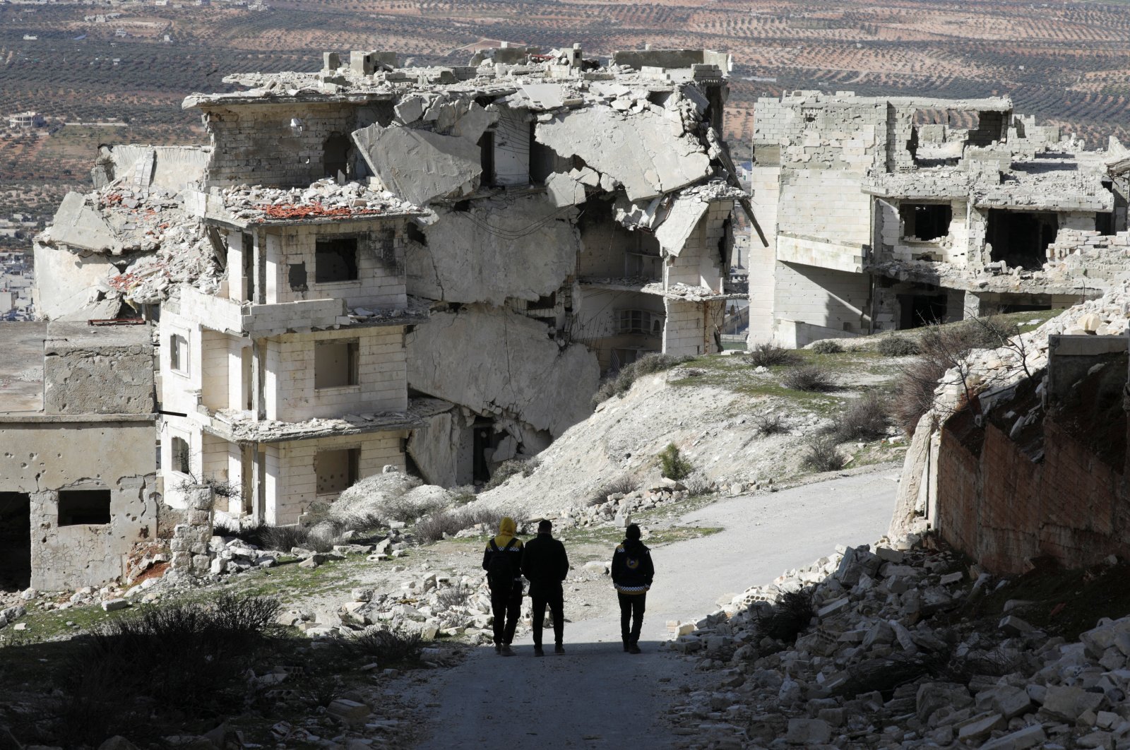 People walk past damaged buildings in the opposition-held Jabal al-Arbaeen, in the southern province of Idlib, northwestern Syria, March 20, 2022. (REUTERS)