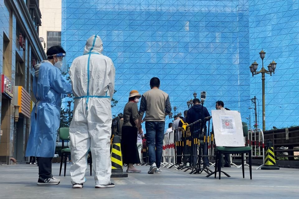 Workers in protective suits stand next to people lining up at a makeshift nucleic acid testing site during mass testing for COVID-19 in the Chaoyang district of Beijing, China, May 4, 2022. (Reuters Photo)