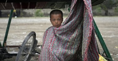 A child shelters from the rain under a wheelbarrow in the city of Kabul, Afghanistan, May 3, 2022. (AP Photo)