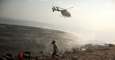 A Frontex helicopter patrols over a Syrian child that has just arrived at a beach on the Aegean island of Lesbos, Greece, Aug. 10, 2015. (Reuters Photo)