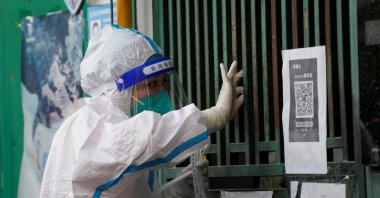 A medical worker in a protective suit collects a swab sample from a resident for nucleic acid testing, outside a closed entrance of a building during a lockdown, amid the coronavirus pandemic, in Shanghai, China, May 5, 2022. (Reuters Photo)