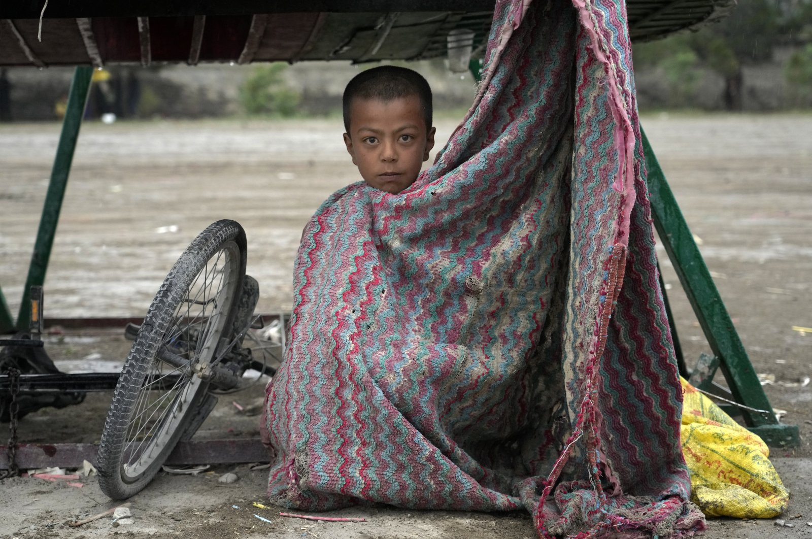 A child shelters from the rain under a wheelbarrow in the city of Kabul, Afghanistan, May 3, 2022. (AP Photo)