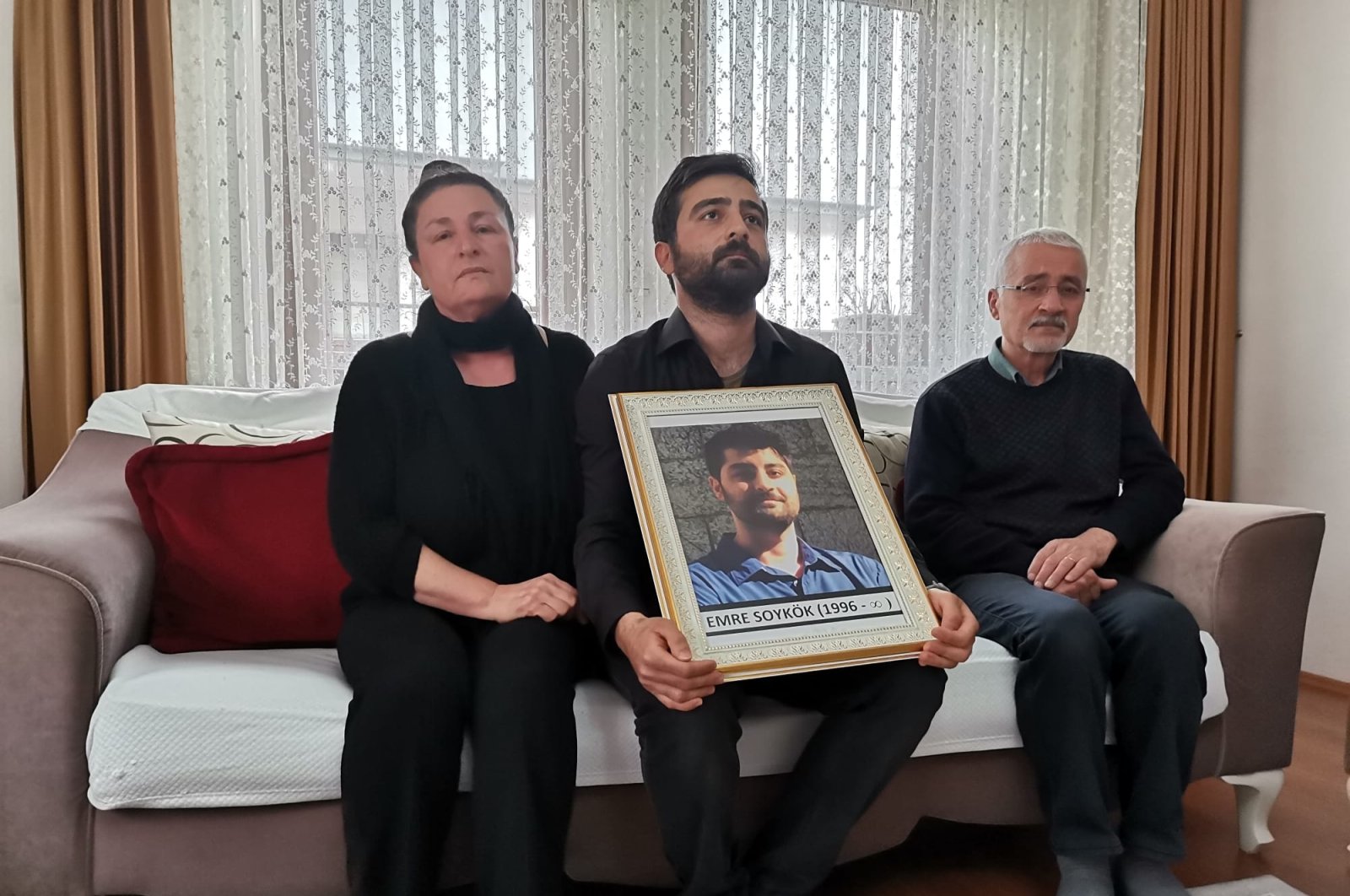 Emre Soykök&#039;s mother, brother and father pose with a photo of the young man in their home, in the capital Ankara, Turkey, May 5, 2022. (DHA PHOTO) 