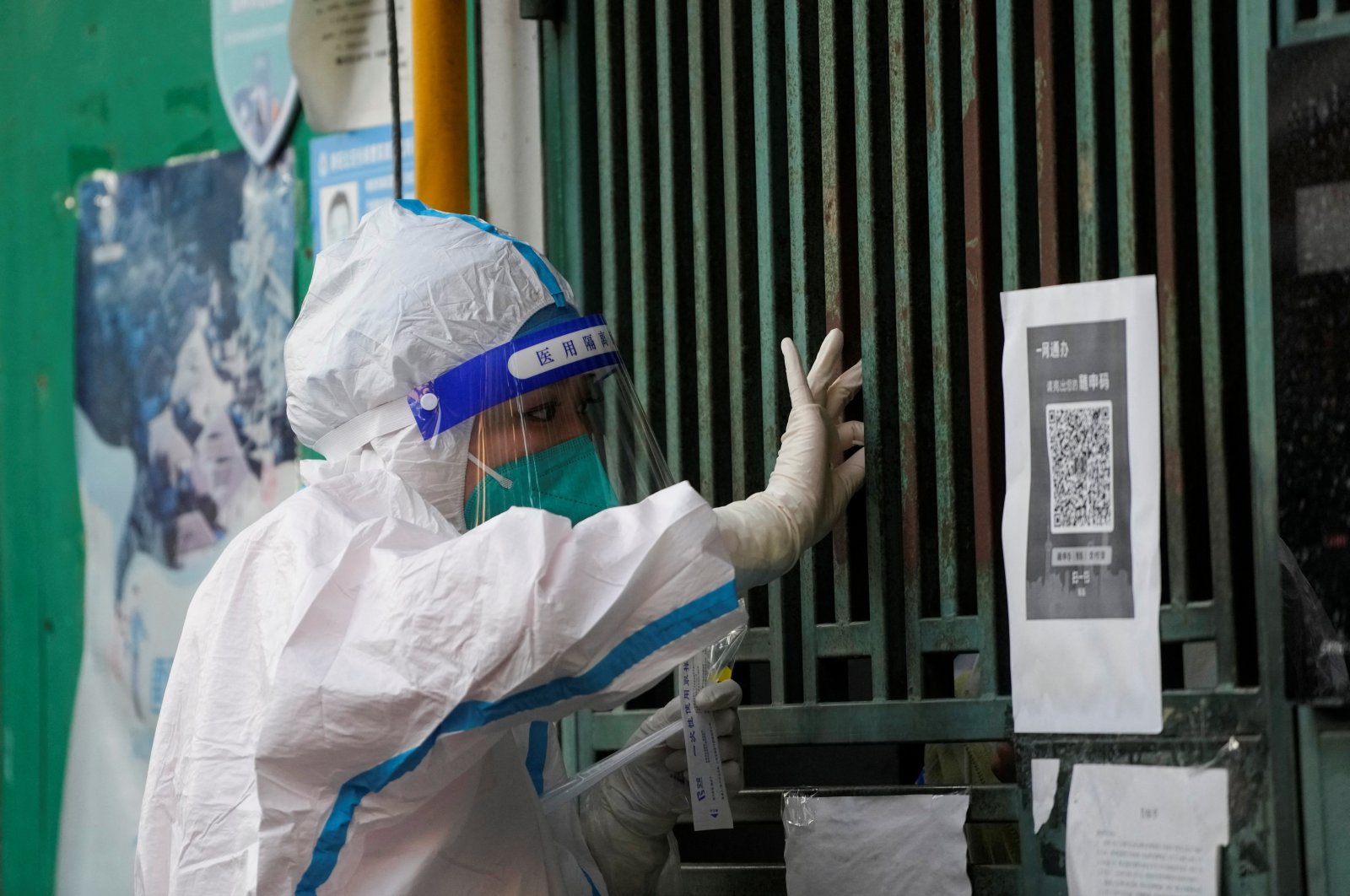 A medical worker in a protective suit collects a swab sample from a resident for nucleic acid testing, outside a closed entrance of a building during a lockdown, amid the coronavirus pandemic, in Shanghai, China, May 5, 2022. (Reuters Photo)