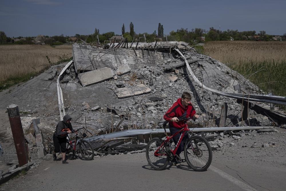 Teenagers on bicycles pass a bridge destroyed by shelling near Orihiv, Ukraine, May 5, 2022. (AP Photo)