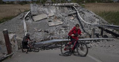 Teenagers on bicycles pass a bridge destroyed by shelling near Orihiv, Ukraine, May 5, 2022. (AP Photo)