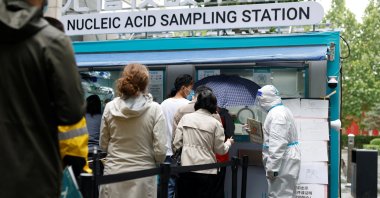 People line up to get tested next to a staff member wearing personal protective equipment (PPE) at a mobile nucleic acid testing site outside a shopping mall, amid the coronavirus disease (COVID-19) outbreak in Beijing, China, May 6, 2022. (Reuters Photo)