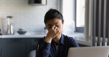 Exhausted young woman working on computer takes off glasses possibly suffering from migraine or headache. (Shutterstock Photo)