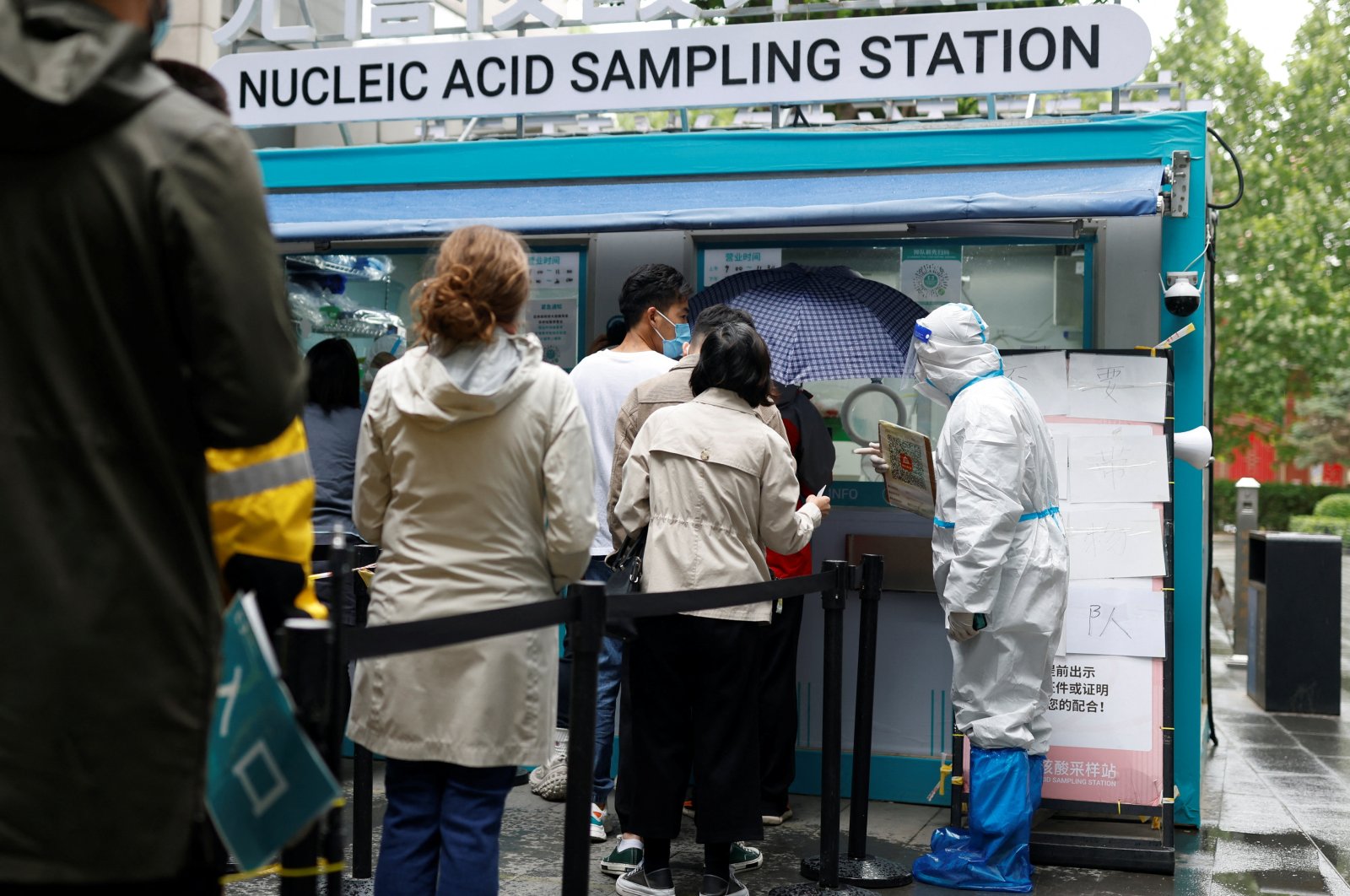 People line up to get tested next to a staff member wearing personal protective equipment (PPE) at a mobile nucleic acid testing site outside a shopping mall, amid the coronavirus disease (COVID-19) outbreak in Beijing, China, May 6, 2022. (Reuters Photo)