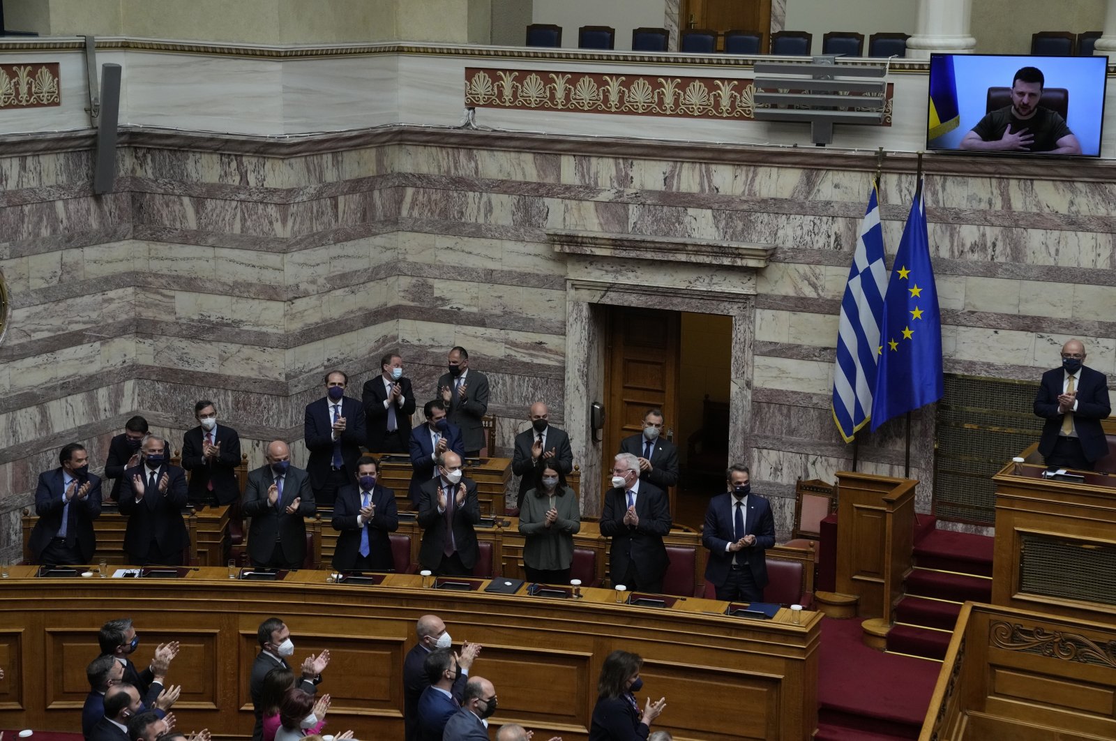Greek Cabinet and lawmakers applaud as Ukrainian President Volodymyr Zelenskyy (on screen) after addressing the Greek Parliament. Zelenskyy called for more weapons to be sent from the West to Ukraine, and for tightened sanctions on Russia, Athens, Greece, April 7, 2022. (AP Photo)