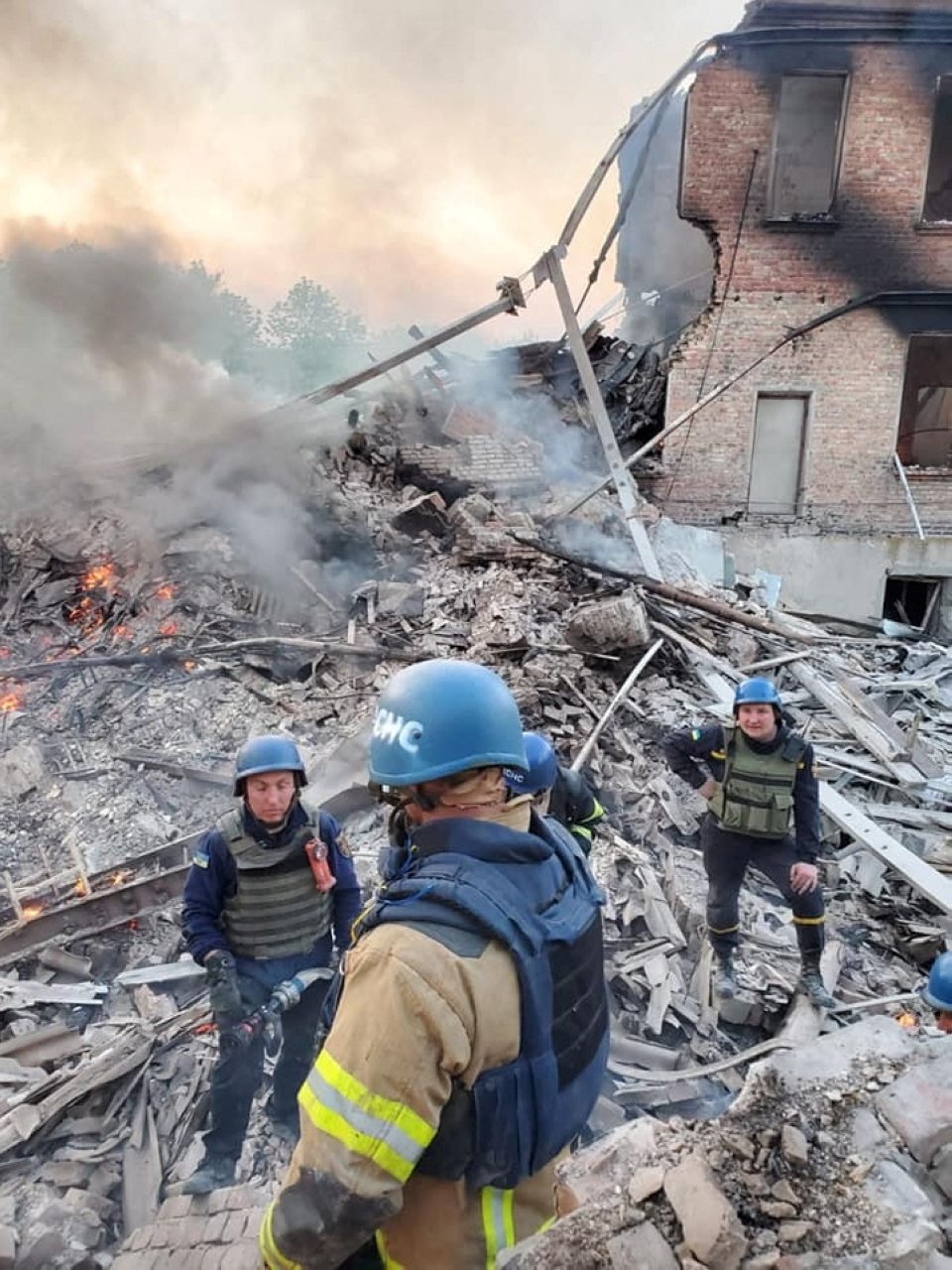 Emergency crew members stand around near burning debris after a school building was hit as a result of shelling, in the village of Bilohorivka, Luhansk, Ukraine, May 7, 2022. (State Emergency Services Handout via Reuters)