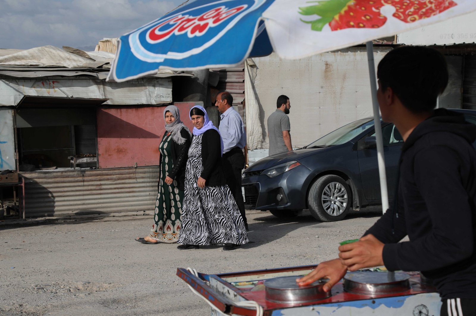 Displaced Yazidi women walk past a street vendor at the Chamishko camp for internally displaced persons in the city of Zakho, northern Iraq, May 5, 2022. (AFP)