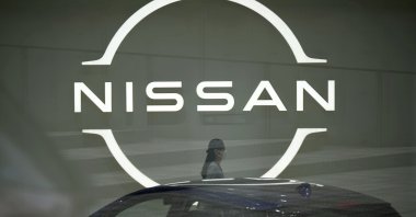 A staff walking near a Nissan logo at Nissan headquarters is seen though a window in Yokohama near Tokyo, Japan, May, 12, 2022. (AP Photo)