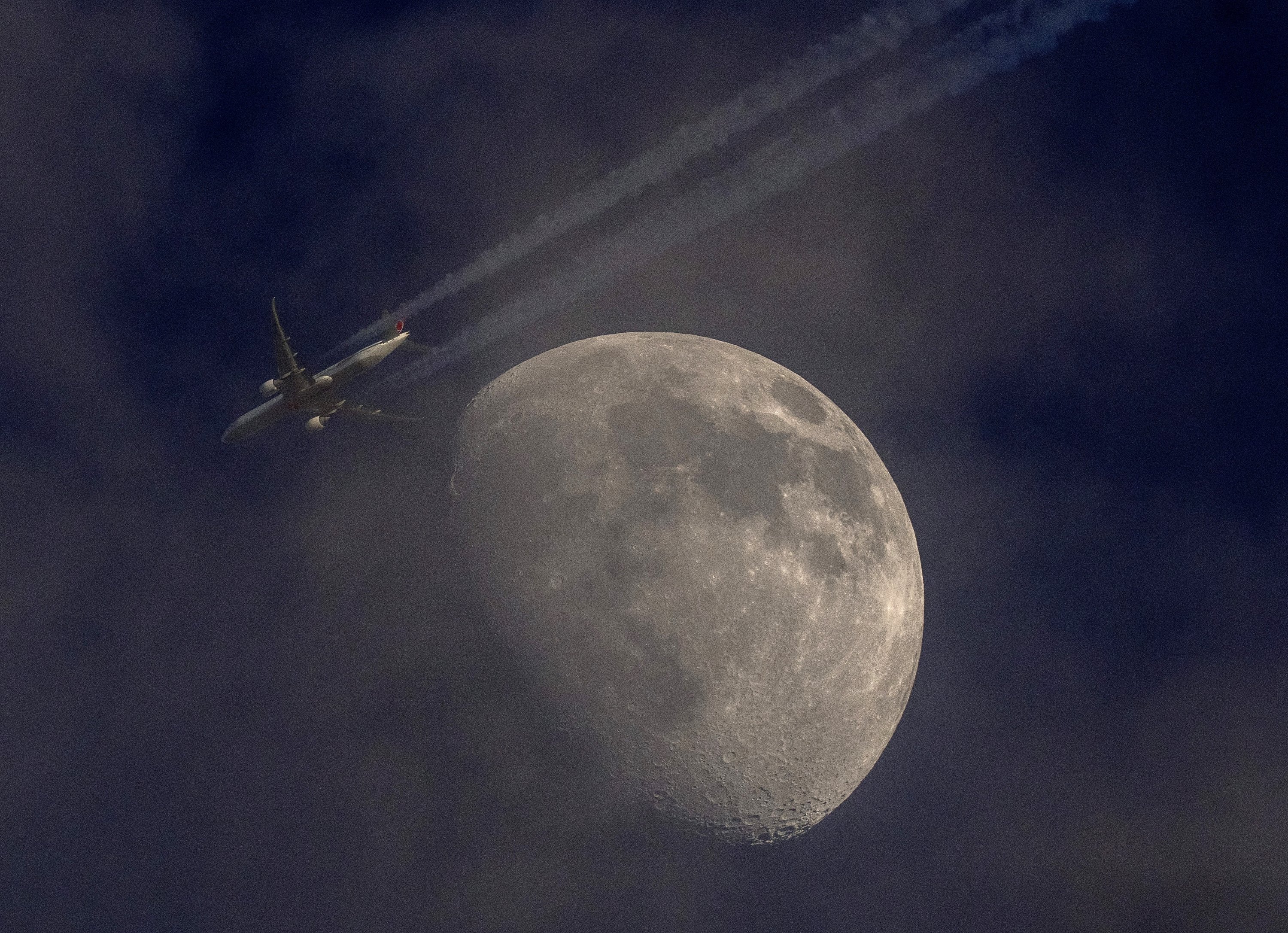Sebuah pesawat melewati bulan yang sedikit tertutup awan di Frankfurt, Jerman, 11 Mei 2022. (AP Photo)