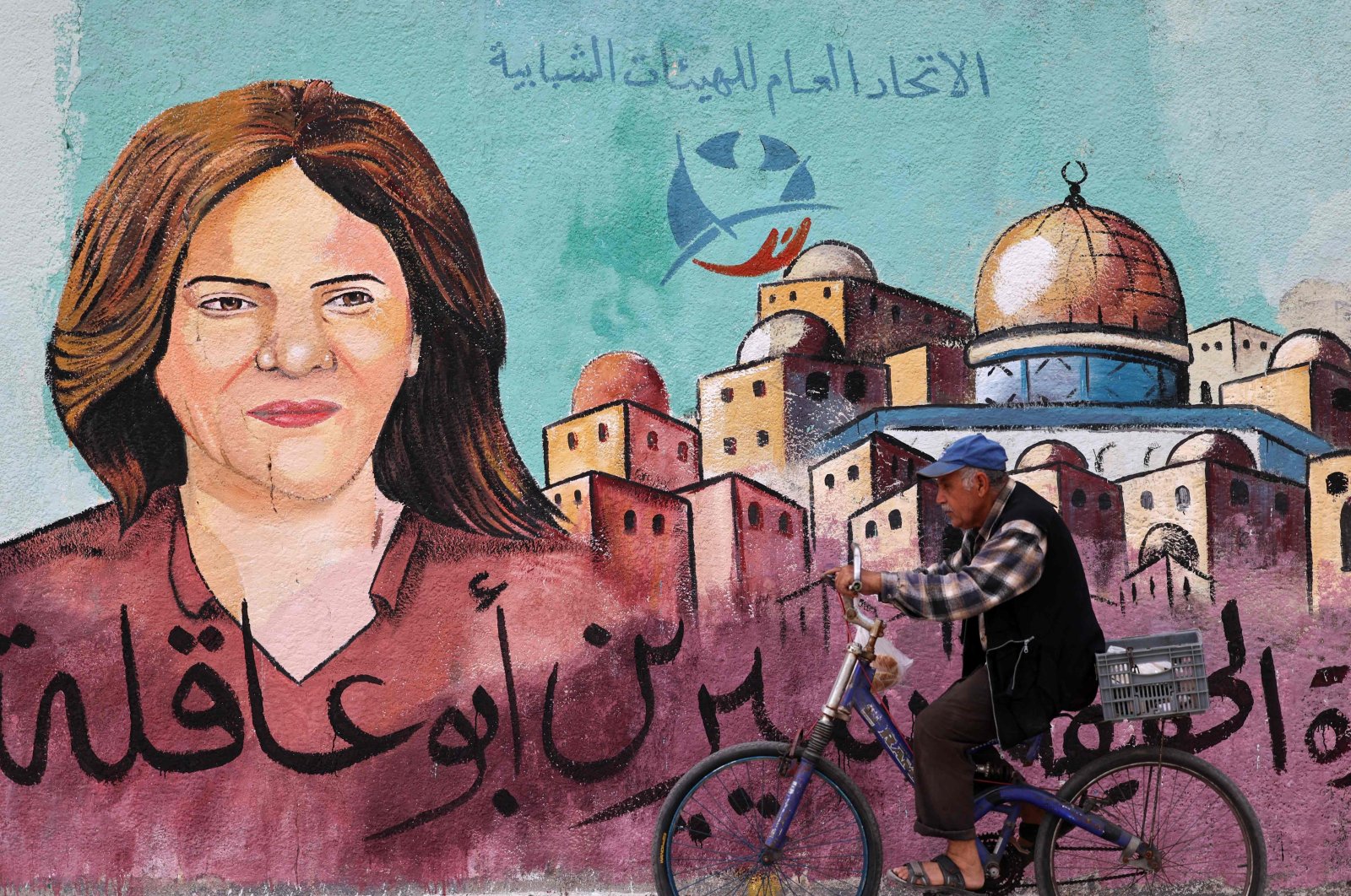 A Palestinian man rides his bicycle in front of a mural painted by an artist in honour of slain veteran Al-Jazeera journalist Shireen Abu Akleh, Gaza City, May 13, 2022. (AFP Photo)