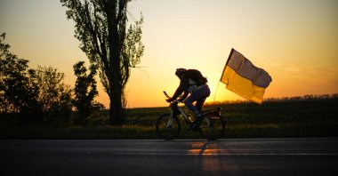 A man rides a bicycle with a Ukrainian flag on the road between Odessa and Mykolaiv, southern Ukraine, May 14, 2022. (AP Photo)