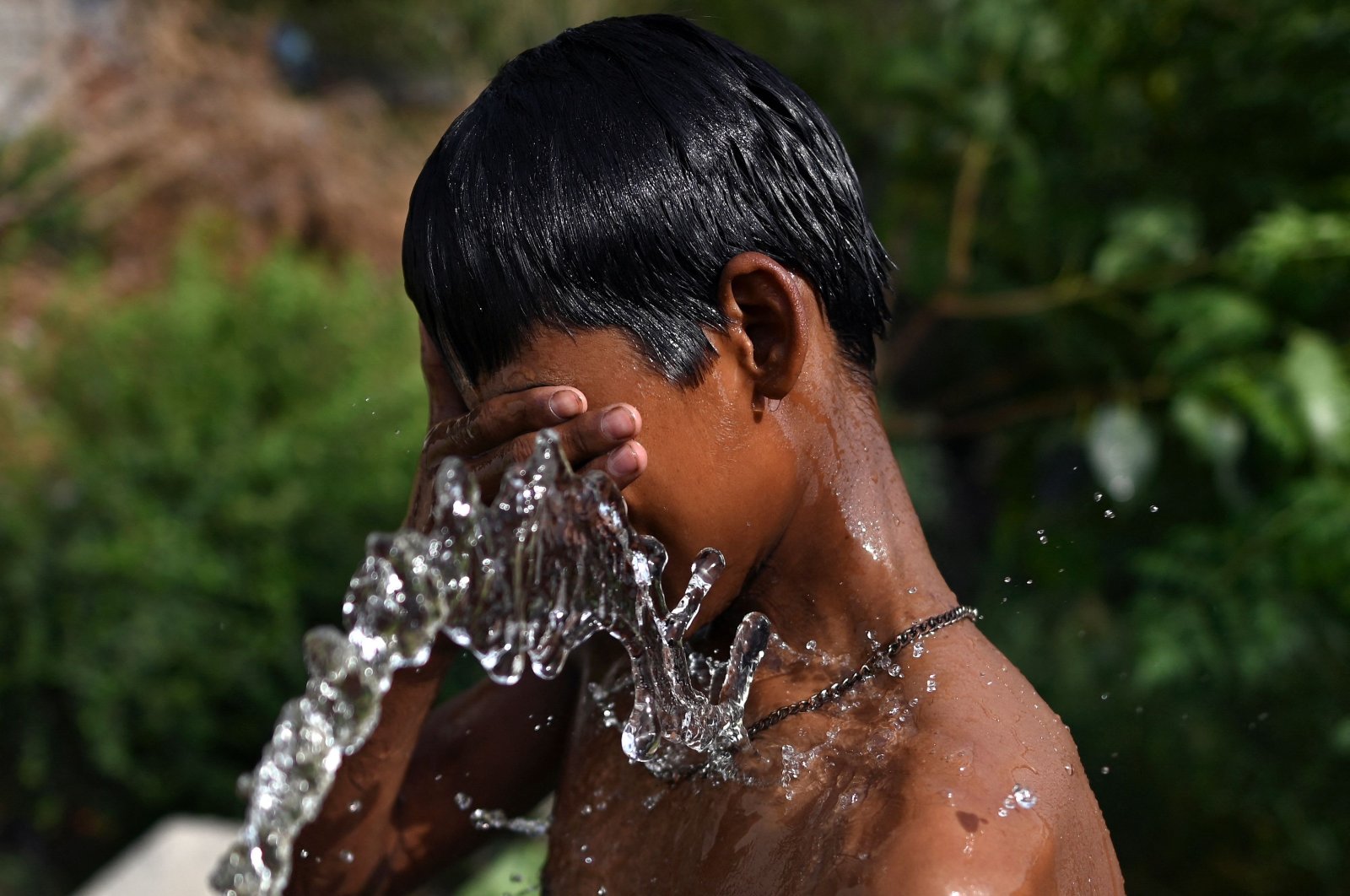 A boy uses a water pipe to bathe on a hot summer day in New Delhi, India, May 15, 2022. (AFP Photo)