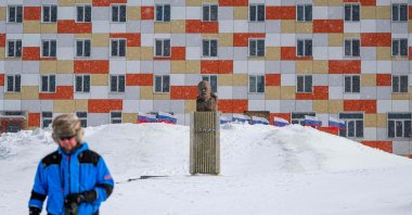 A man walks on the snow past a monument to Lenin in front of a building with Russian flags flapping in the blizzard, in the miners&#039; town of Barentsburg, Svalbard Archipelago, northern Norway, May 7, 2022. (AFP Photo)