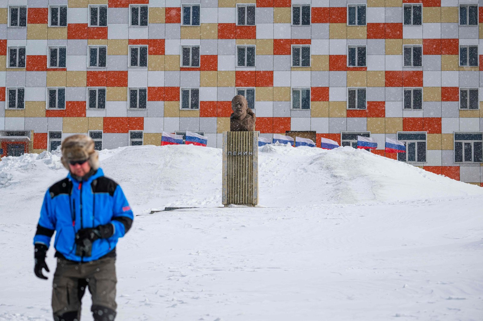 A man walks on the snow past a monument to Lenin in front of a building with Russian flags flapping in the blizzard, in the miners&#039; town of Barentsburg, Svalbard Archipelago, northern Norway, May 7, 2022. (AFP Photo)