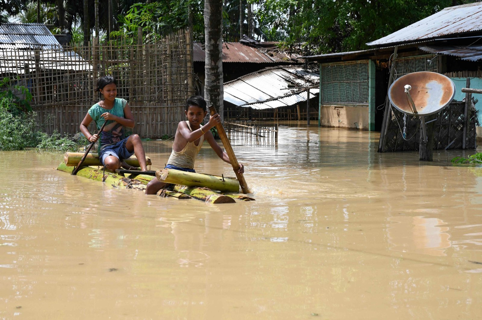 Children ride a bamboo raft through a flooded area after heavy rains in Morigaon district of Assam state, India, May 22, 2022. (AFP Photo)
