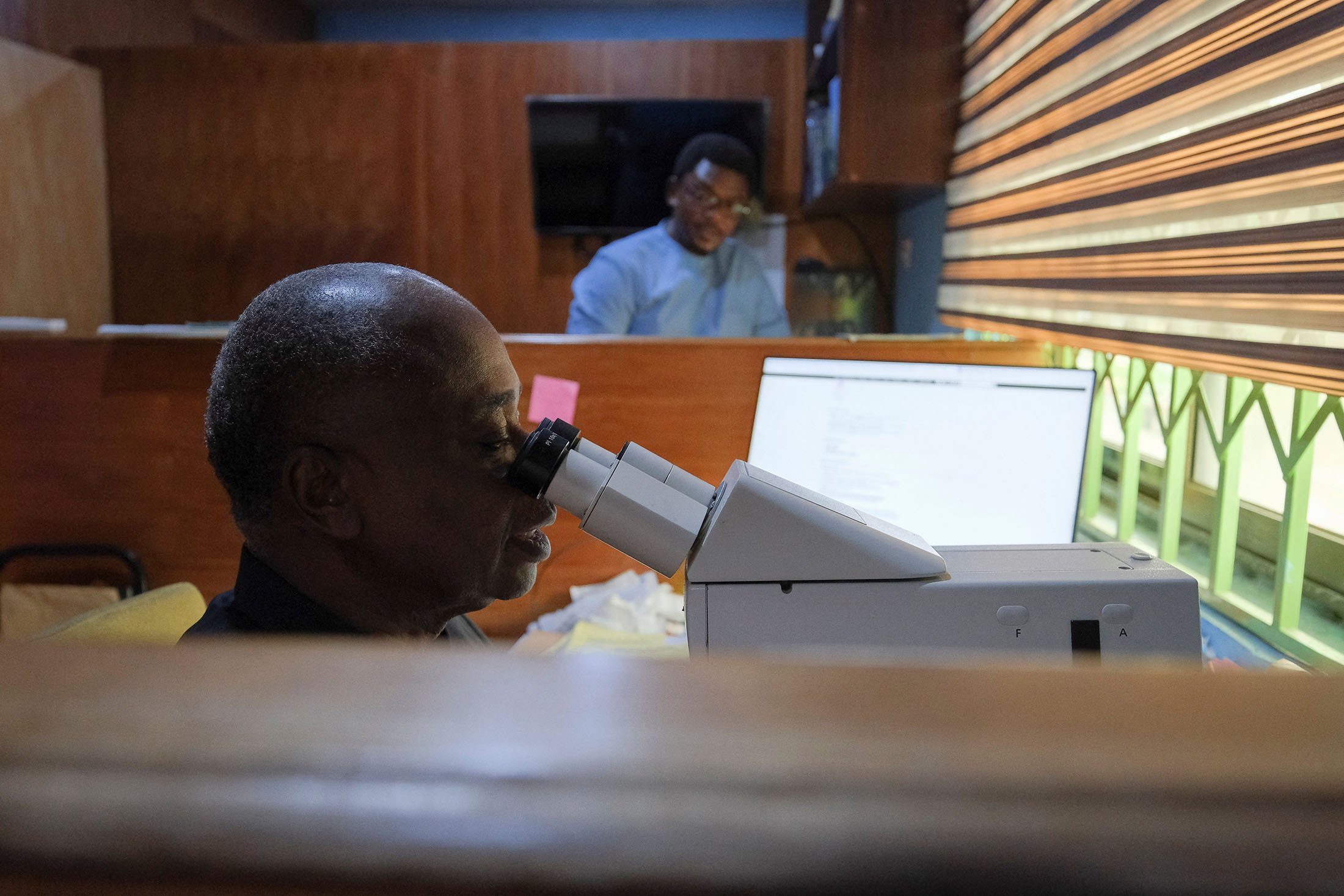 Lawrence Adusei, 64, seorang ahli patologi, mengamati slide melalui mikroskop di laboratorium Pathologists Without Borders di Accra, Ghana, 16 Mei 2022. (Foto Reuters)