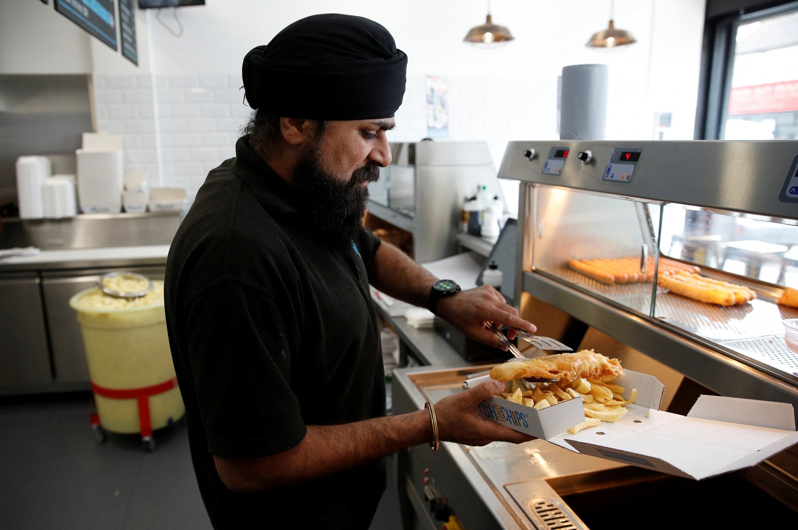 The owner of Hooked Fish and Chips shop, Bally Singh, prepares a portion of fish and chips at his takeaway in West Drayton, Britain, May 25, 2022. (Reuters Photo)