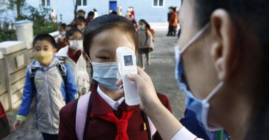 A teacher takes the body temperature of a schoolgirl to help curb the spread of the coronavirus before entering Kim Song Ju Primary School in Central District in Pyongyang, North Korea, Oct. 13, 2021. (AP Photo)