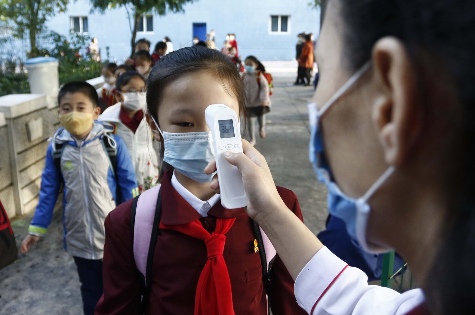 A teacher takes the body temperature of a schoolgirl to help curb the spread of the coronavirus before entering Kim Song Ju Primary School in Central District in Pyongyang, North Korea, Oct. 13, 2021. (AP Photo)