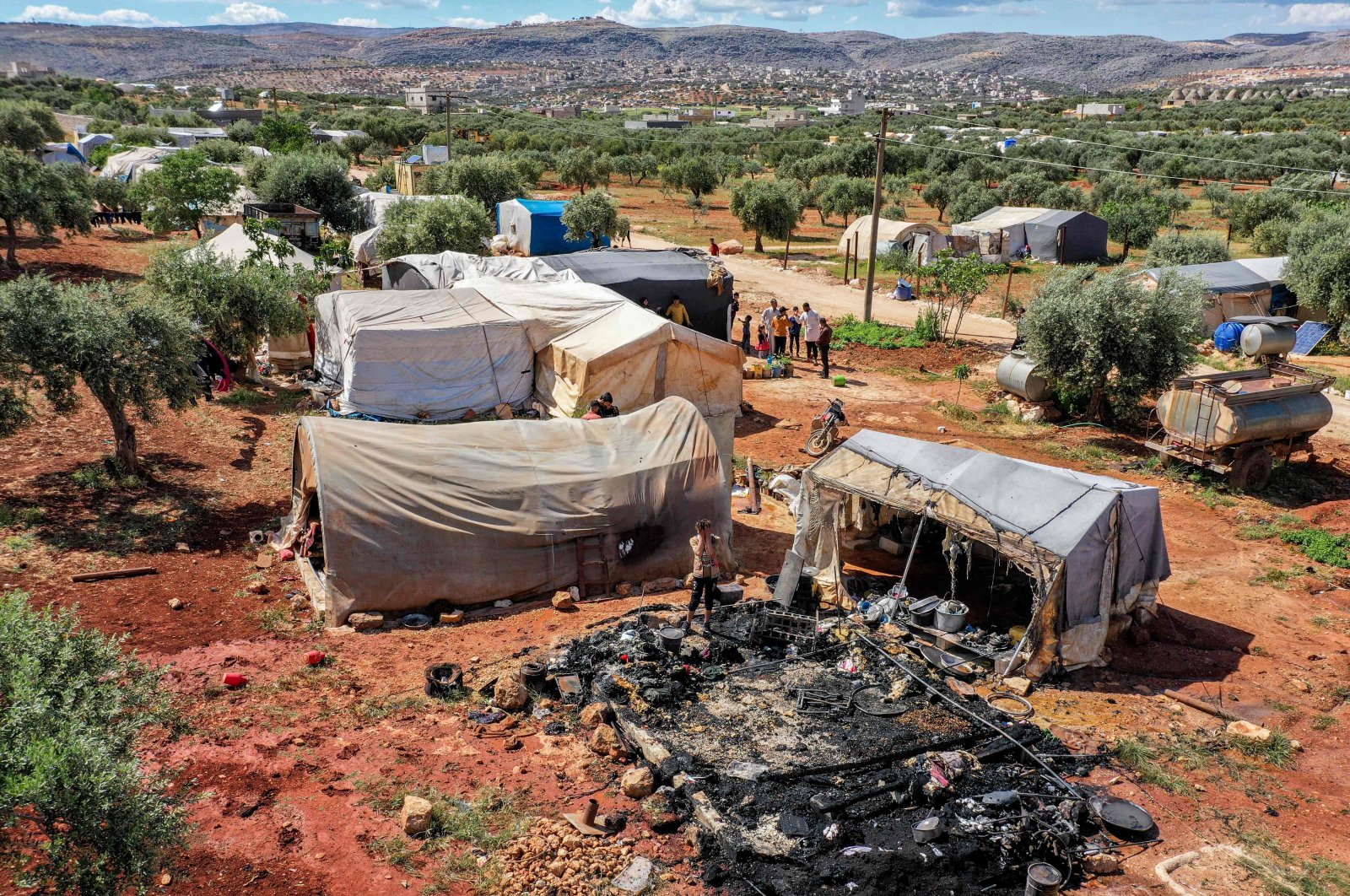 This picture taken on May 7, 2022, shows an aerial view of a young Syrian standing near the remains of a burnt-down tent following a fire caused by the malfunctioning battery of a solar panel, at a camp for Syrians displaced by the conflict near the village of Haranbush in the opposition-held part of the northwestern province of Idlib province. (AFP Photo)