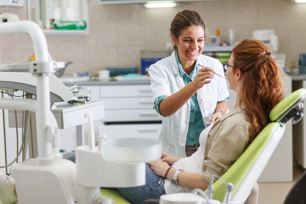 A dentist in a dental office talks with a patient and prepares to administer treatment. (Shutterstock Photo)