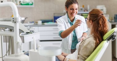 A dentist in a dental office talks with a patient and prepares to administer treatment. (Shutterstock Photo)