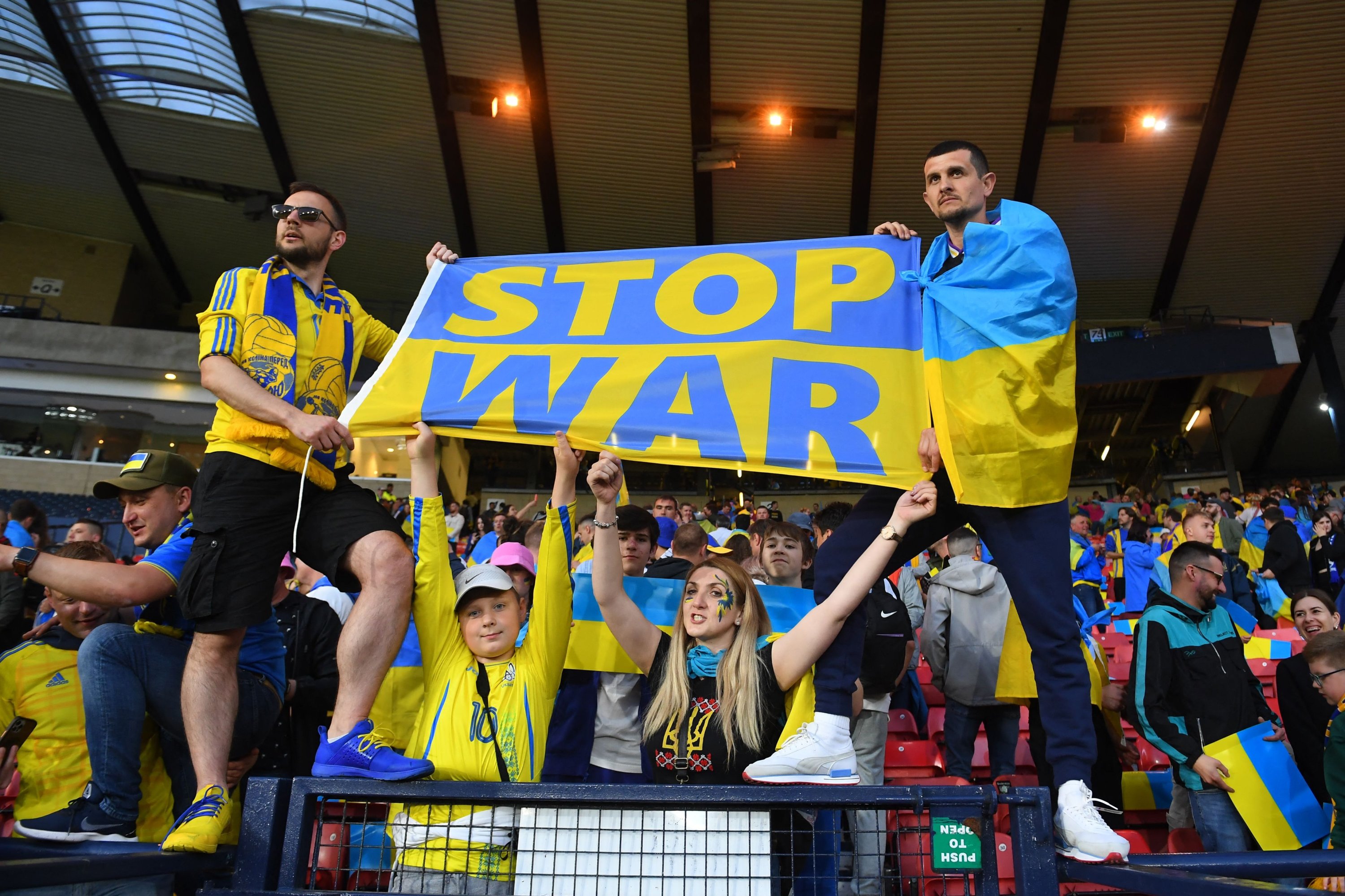 Fans draped in Ukraine national flags hold a banner during the FIFA World Cup 2022 playoff semifinal qualifier football match between Scotland and Ukraine at Hampden Park in Glasgow, Scotland on June 1, 2022. (AFP Photo)