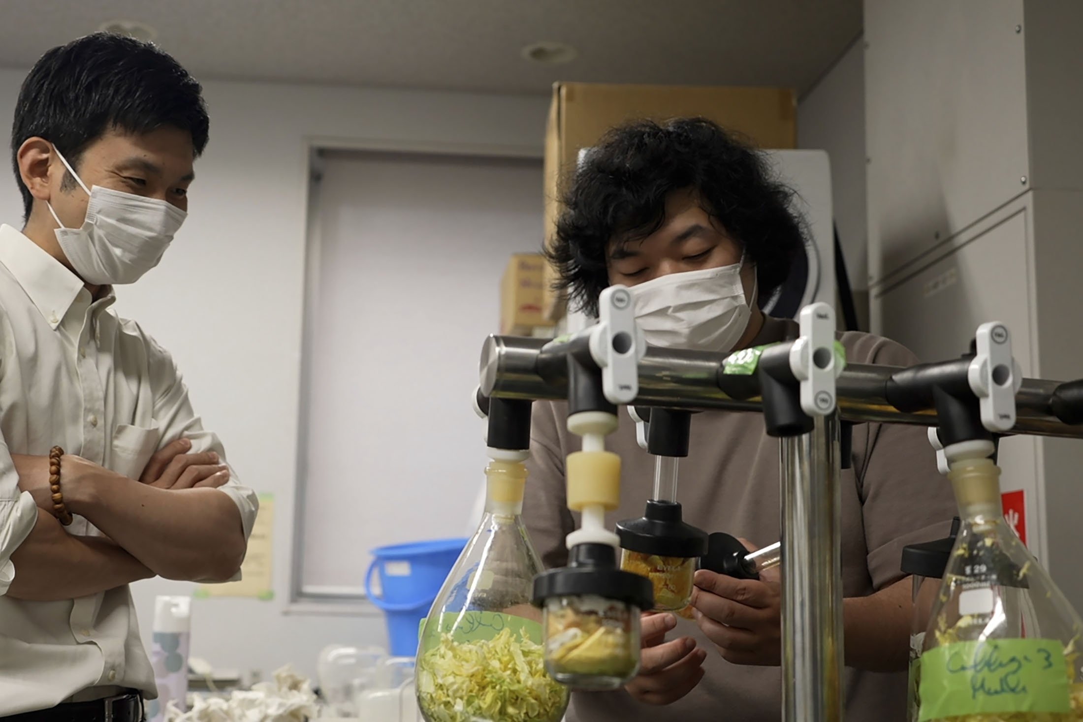 Peneliti Universitas Tokyo Yuya Sakai (kiri), dan Kota Machida, memeriksa sayuran kering dan kulit buah sebelum dihancurkan menjadi partikel di laboratorium universitas mereka di Tokyo, Jepang, 26 Mei 2022. (AP Photo)