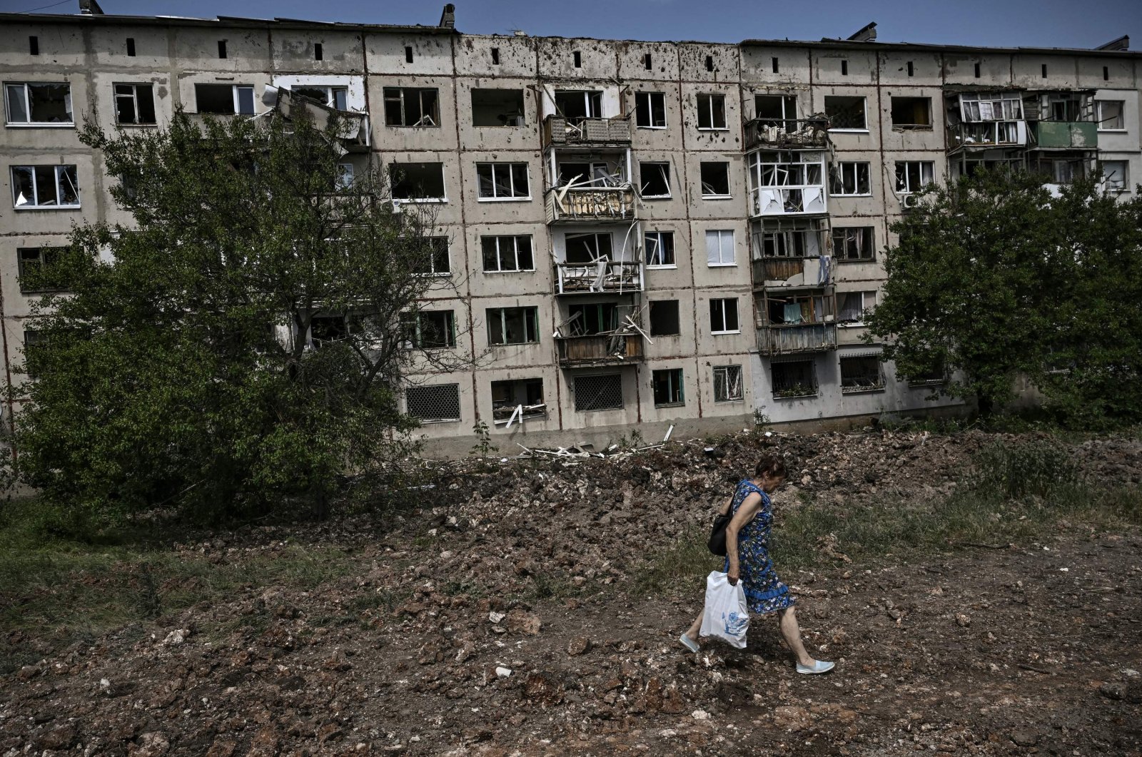 A woman walks in front of a damaged apartment building after a missile strike in the city of Soledar, in the eastern Ukrainian region of Donbass, June 4, 2022. (AFP Photo)