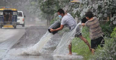 Residents use water to clear ash from the front of their residences in Juban town, Sorsogon Province, after the sudden eruption of Bulusan Volcano, Philippines, June 5, 2022. (AFP Photo)