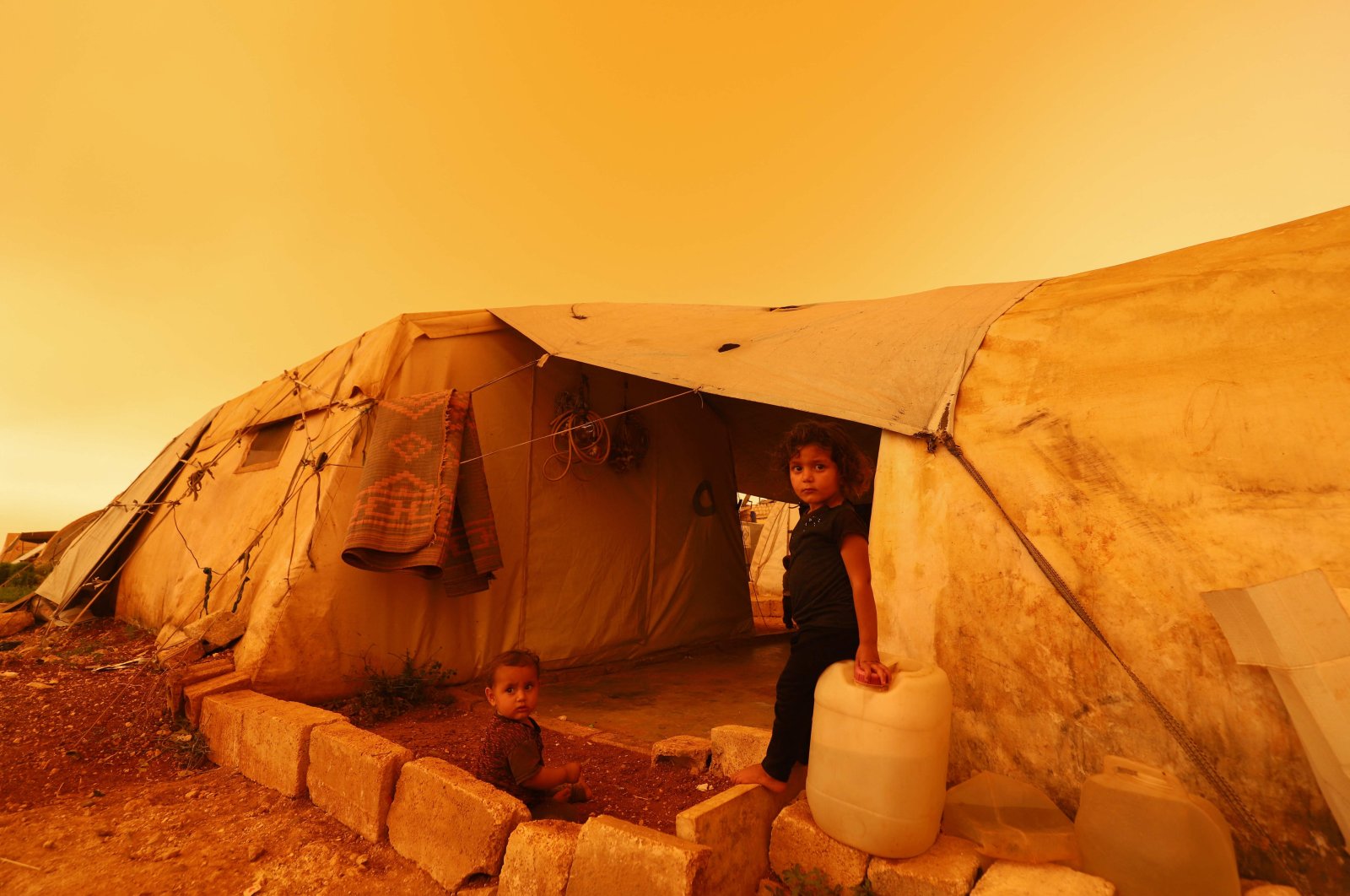 Displaced children sit next to their tent during a dust storm over the town of Zardana in the countryside of Idlib province, northern Syria, June 2, 2022. (AFP Photo)