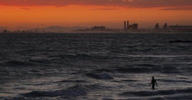A man wades into the ocean at sunset, in Newport Beach, California, U.S., June 22, 2021. (AP Photo)