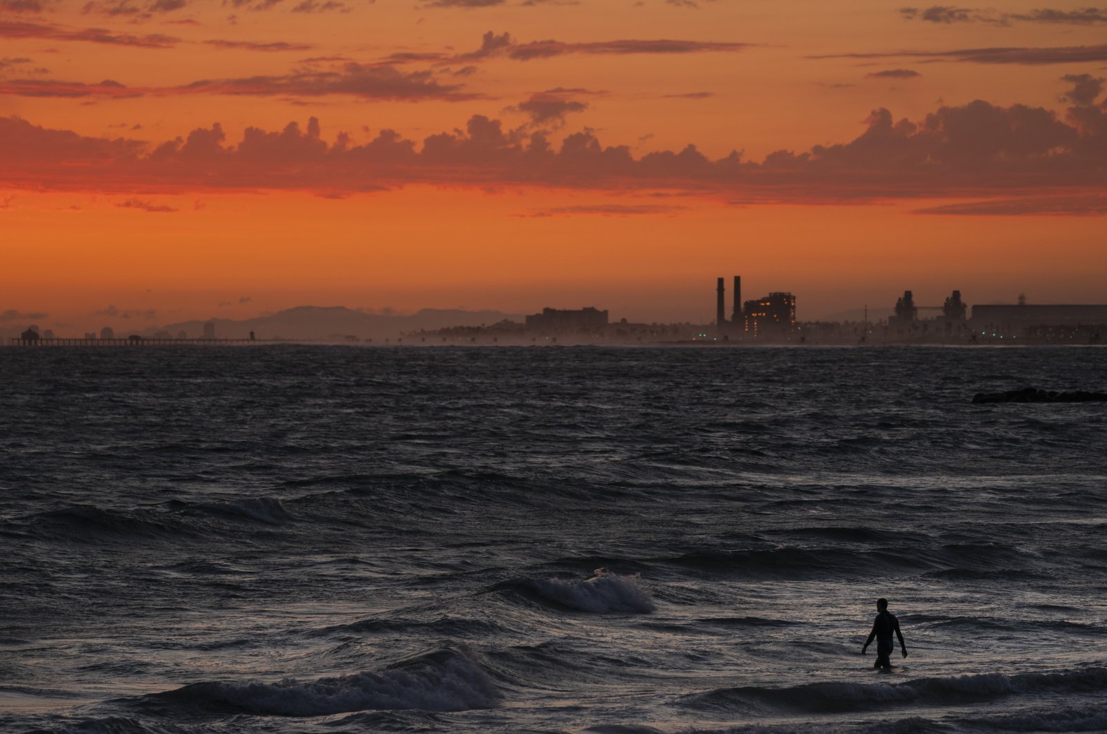 A man wades into the ocean at sunset, in Newport Beach, California, U.S., June 22, 2021. (AP Photo)