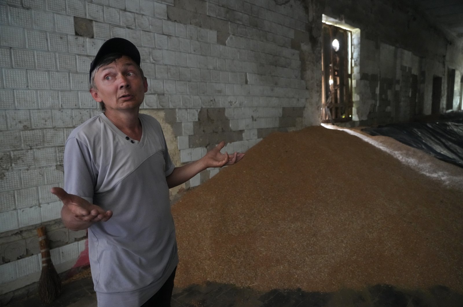 Farmer Serhii gestures while standing near a mound of grain in his barn in the village of Ptyche in the eastern Donetsk region, Ukraine, June 12, 2022. (AP Photo)