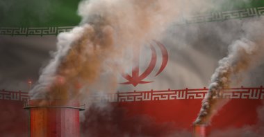 The heavy smoke of factory chimneys is overlaid on Iran&#039;s flag. (ShutterStock Photo)