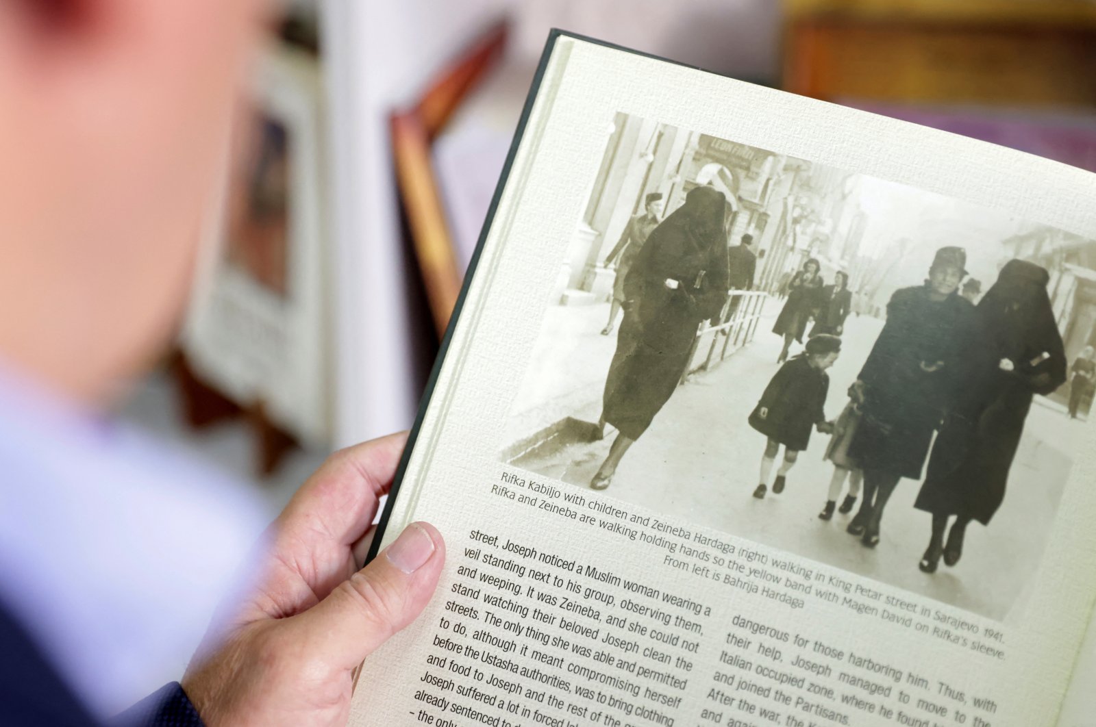 Eli Tauber shows a picture in a book of Rifka Kabiljo and Zeineba Hardaga walking on a street in Sarajevo in 1941, in Sarajevo, Bosnia-Herzegovina, June 13, 2022. (REUTERS)
