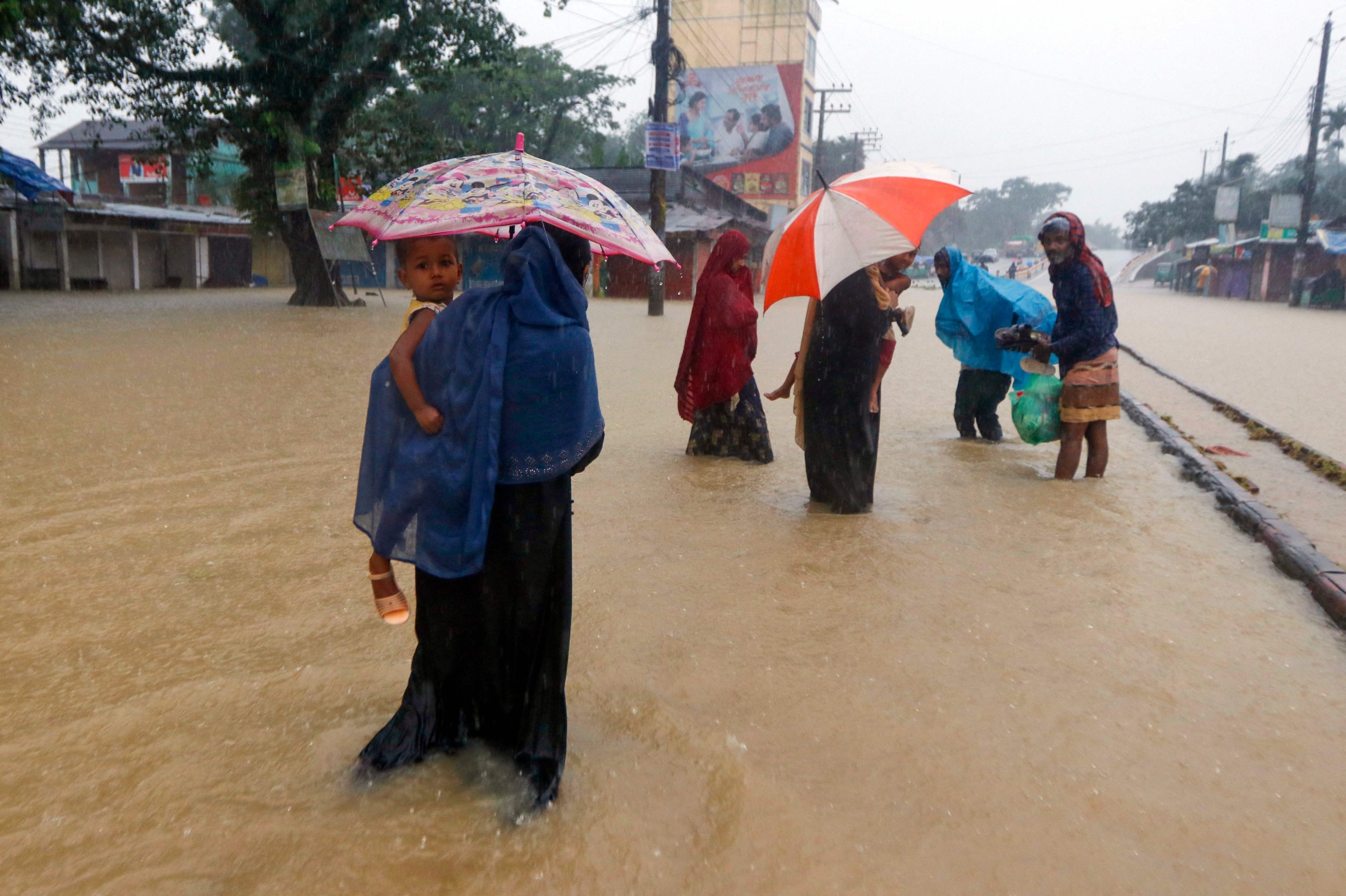 Orang-orang berjalan di sepanjang jalan di daerah banjir setelah hujan lebat di Sylhet, Bangladesh, 18 Juni 2022. (AFP Photo)