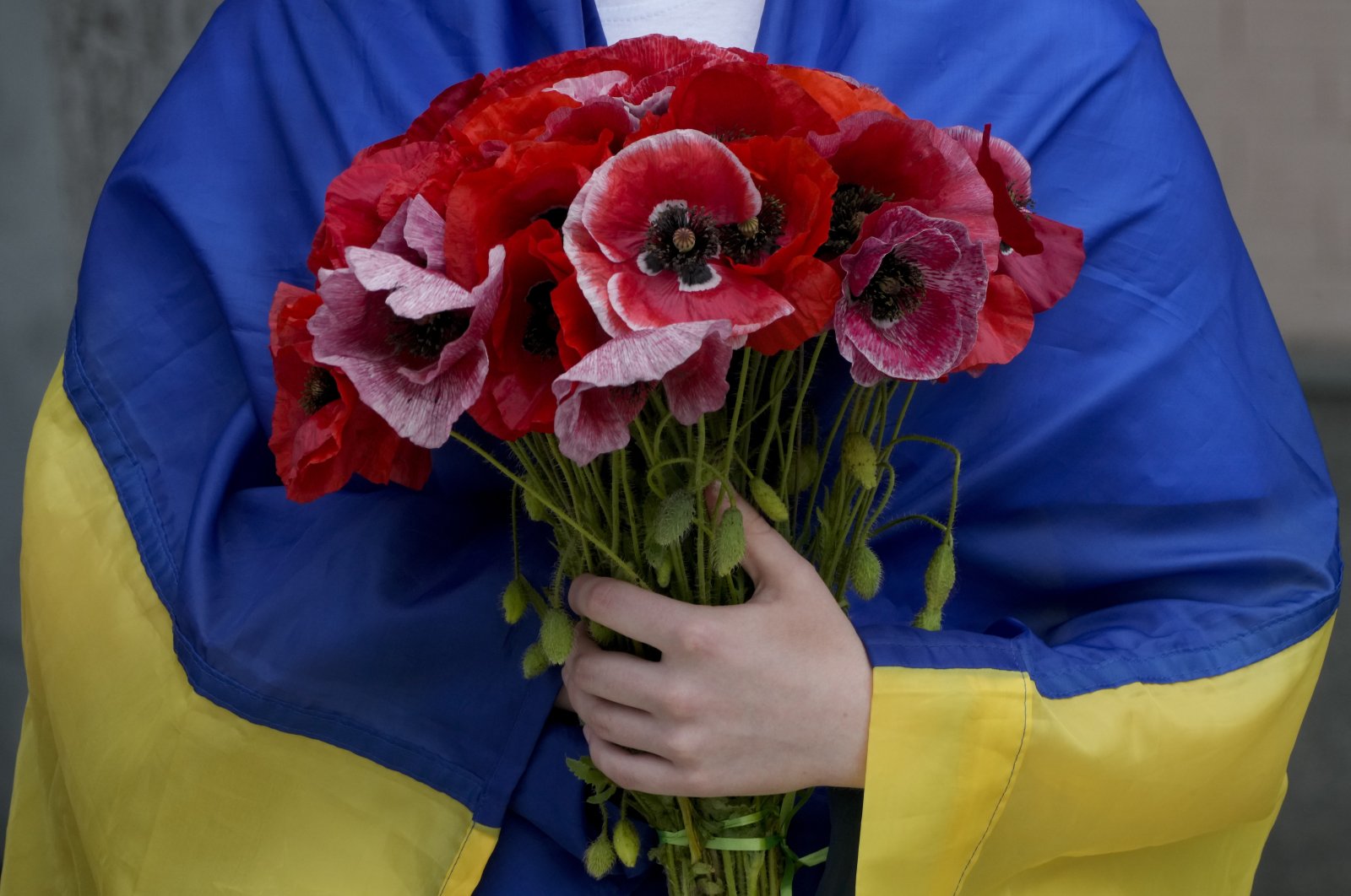 A woman wrapped in a Ukrainian flag holds flowers during the memorial service of activist and soldier Roman Ratushnyi in Kyiv, Ukraine, June 18, 2022. (AP Photo)