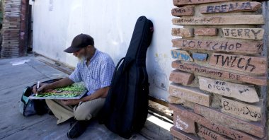 A homeless man works on a sign as he sits next a monument to homeless people who have died Phoenix, Arizona, U.S., April 27, 2022. (AP Photo)
